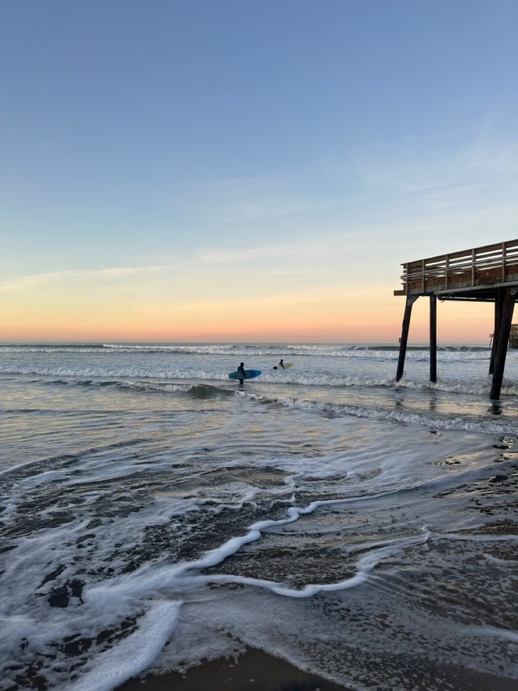 people are swimming in the ocean near a pier at sunset or dawn with surfboards