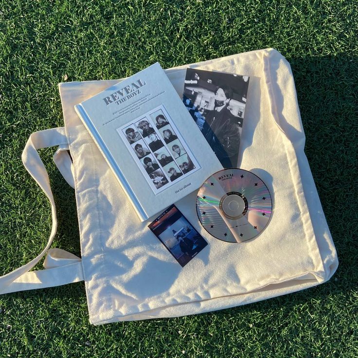 an open book and cd sitting on top of a white bag with grass in the background