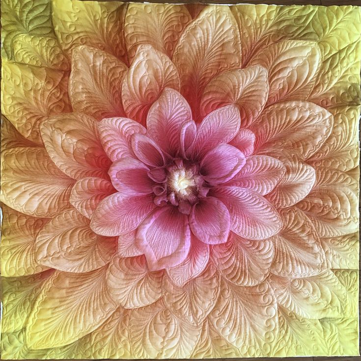 a large pink flower sitting on top of a green and yellow quilted wall hanging