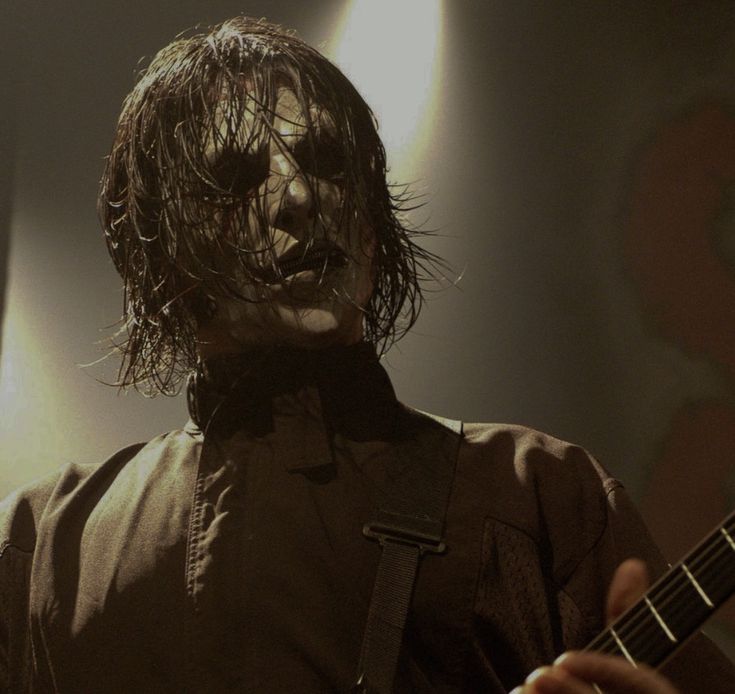 a man with long hair holding a guitar in front of his face and looking at the camera