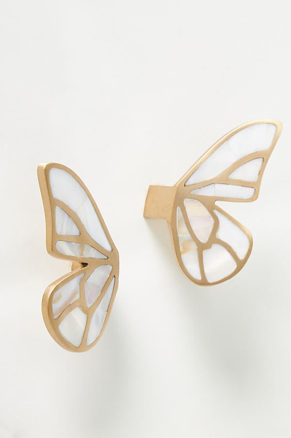 two gold and white butterfly shaped earrings on top of each other, one with its wings open