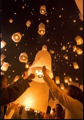 people releasing paper lanterns into the sky at night with their hands in each other's pockets