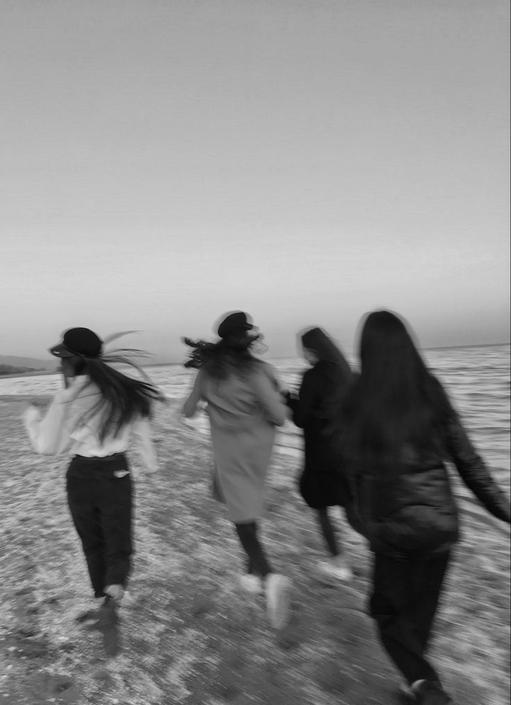 black and white photograph of four women walking on the beach with their hair blowing in the wind