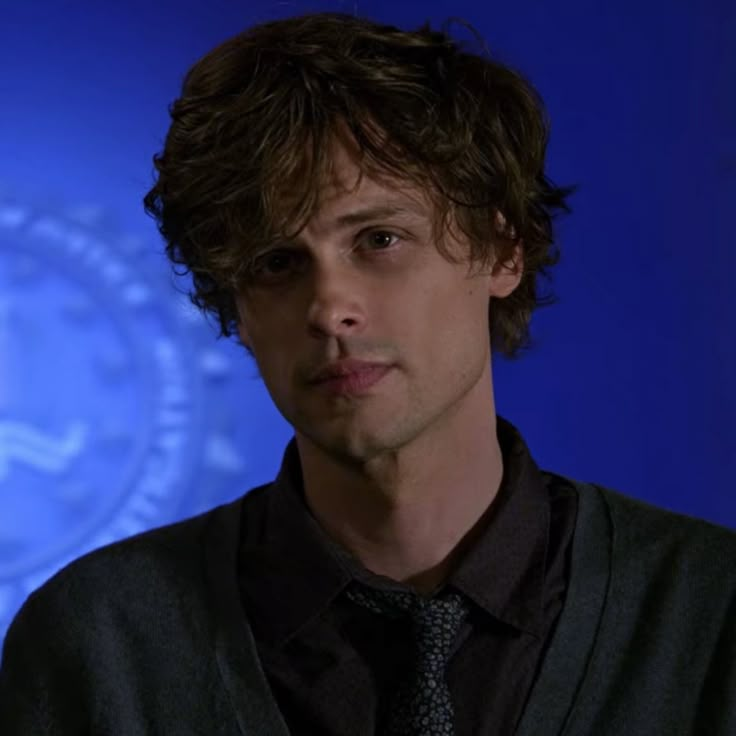 a close up of a person wearing a black shirt and tie in front of a blue background