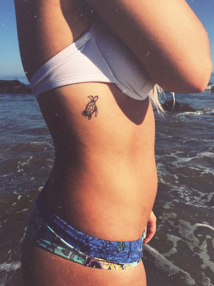 a woman with a small bee tattoo on her stomach standing in the water at the beach