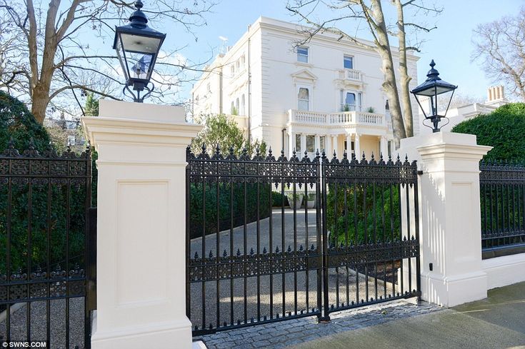 a white house behind a black fence with two lamps on each side and trees in the background