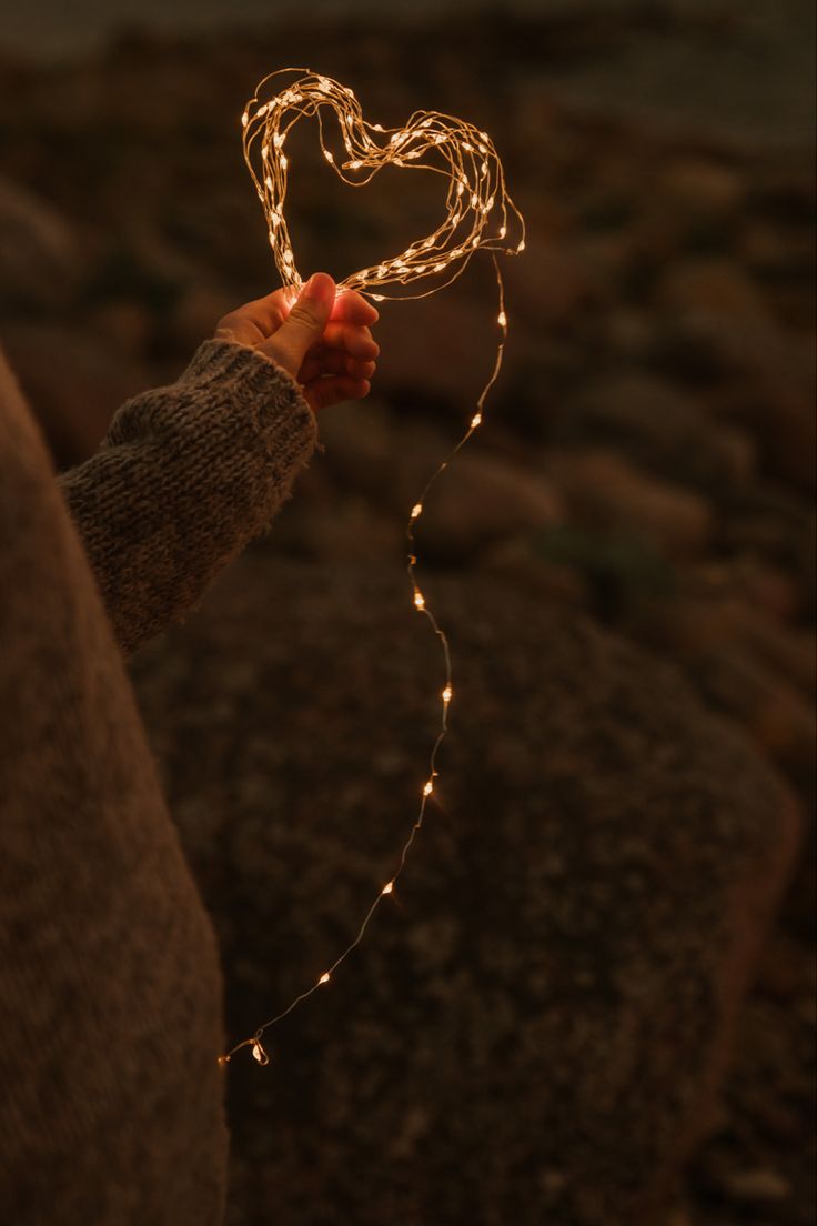 a person holding a string of lights in their hand with a heart shape on it