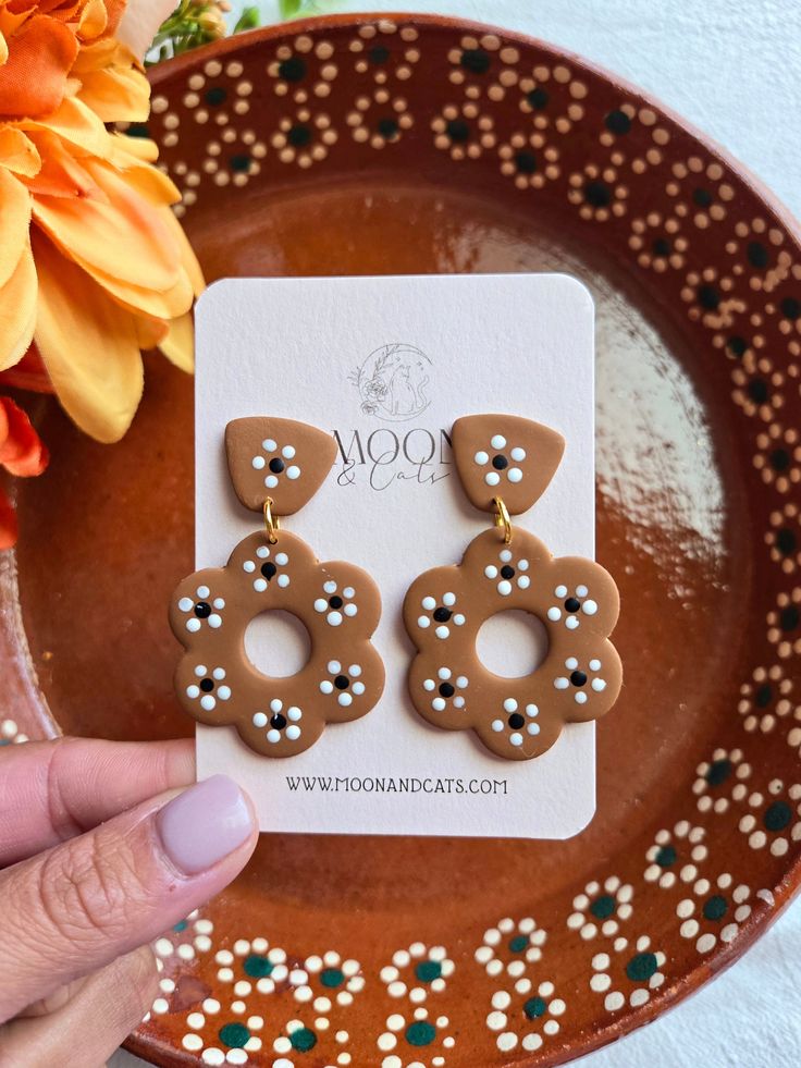 a pair of brown and white earrings sitting on top of a plate next to flowers