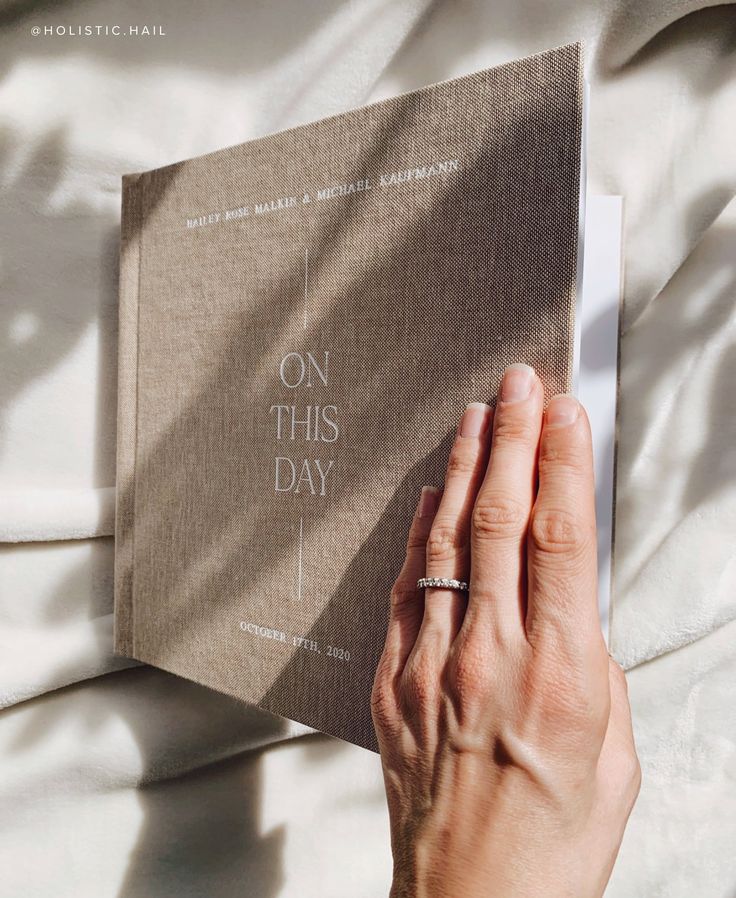 a person is holding up a book on this day with the cover pulled back to reveal their wedding ring