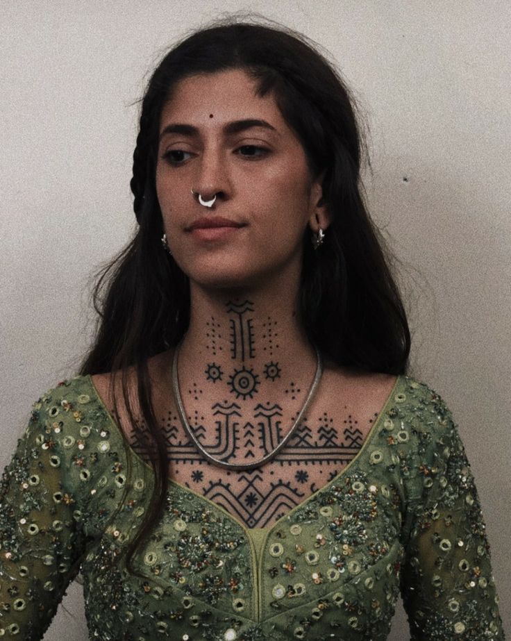 a woman with tattoos on her face and chest standing in front of a white wall