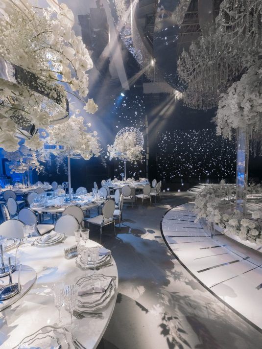 an empty banquet room with white tables and chairs, lit by lights from the ceiling