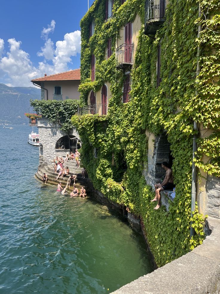 some people are sitting on the edge of a building by the water and there is a boat in the water