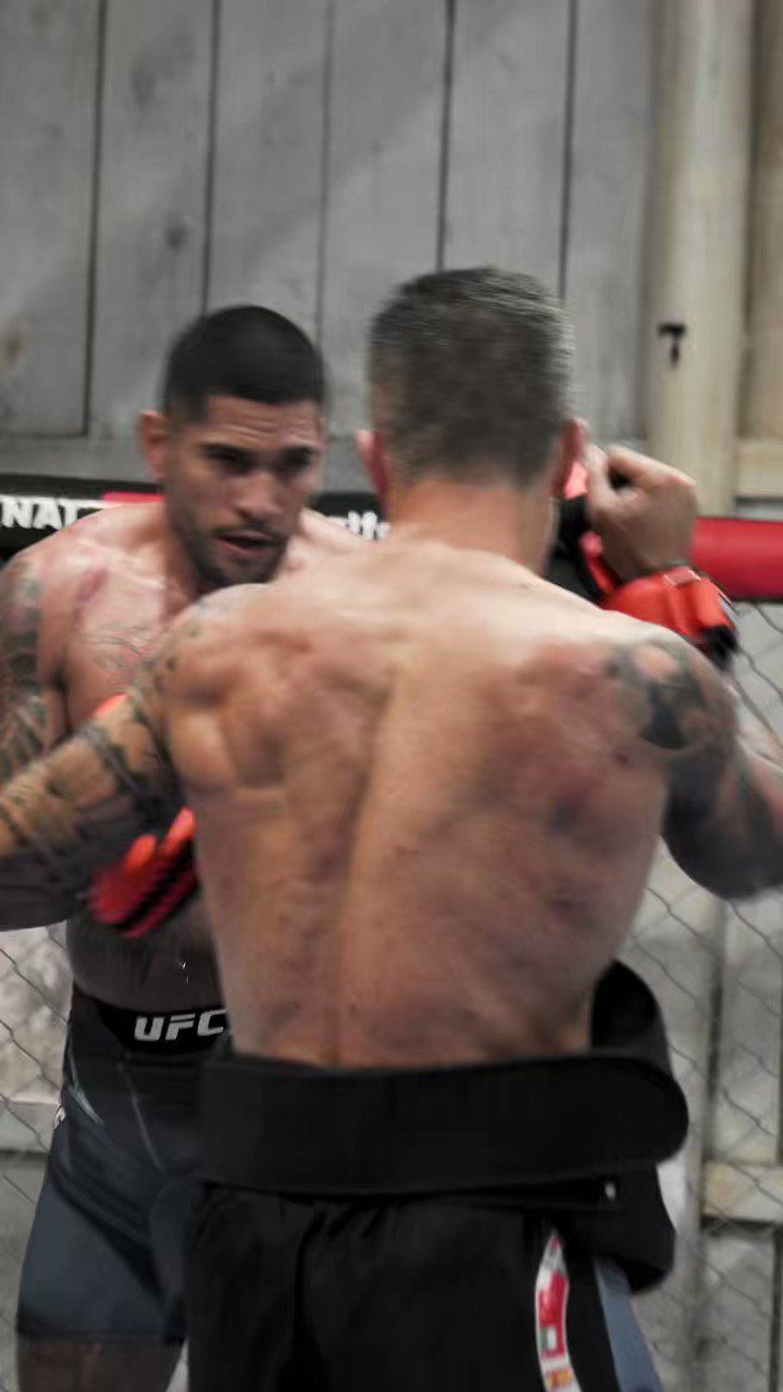 two men standing next to each other in a caged area with one holding a punching bag