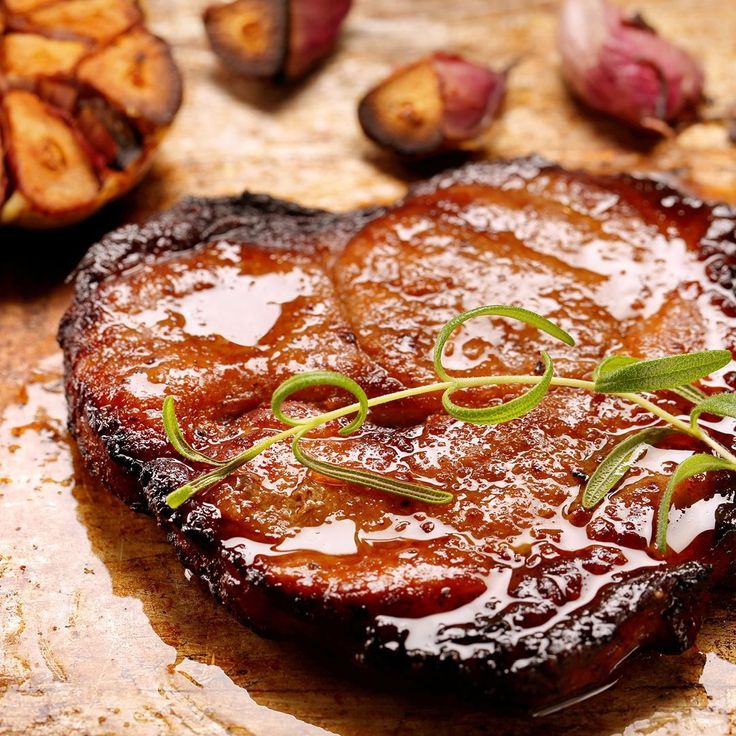 grilled steak with sauce and green garnish on wooden cutting board next to garlic