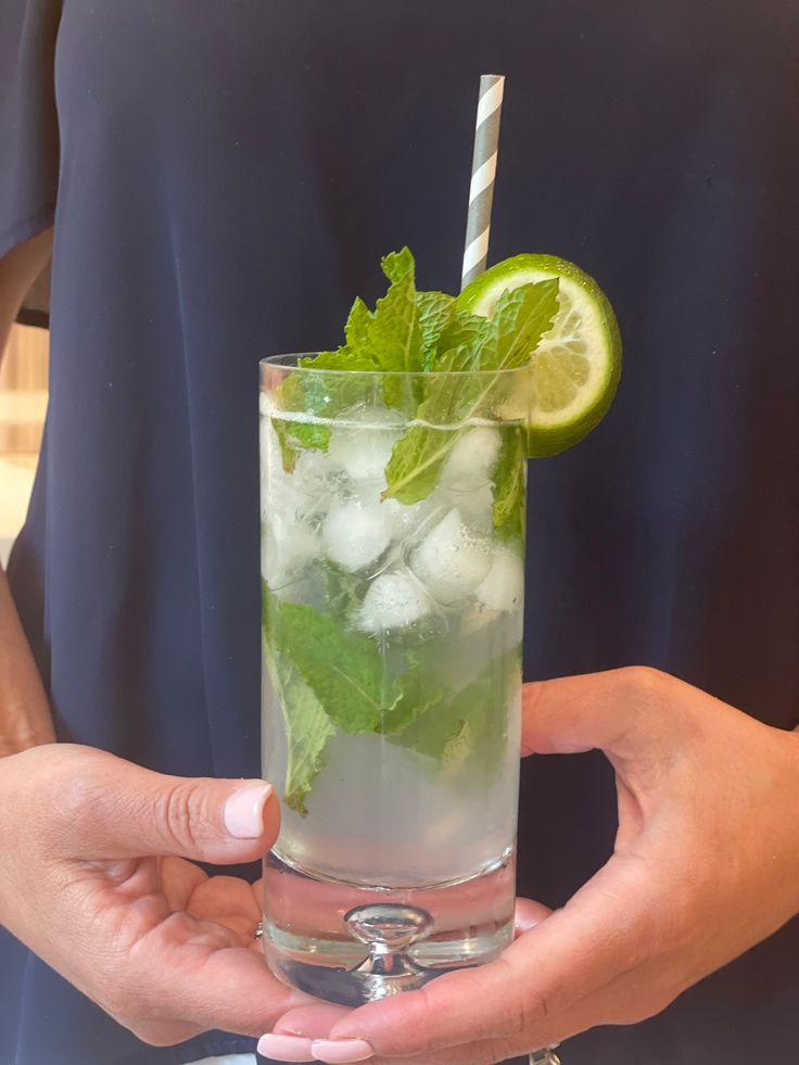 a person holding a tall glass filled with ice and lime