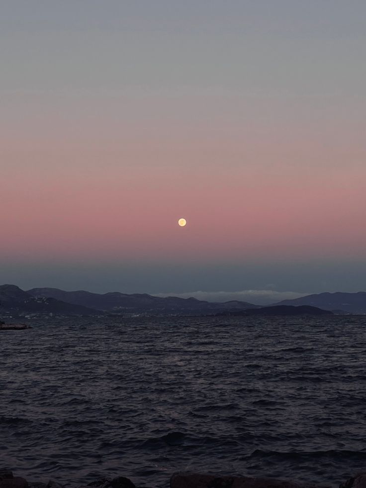 the sun is setting over the ocean with mountains in the background