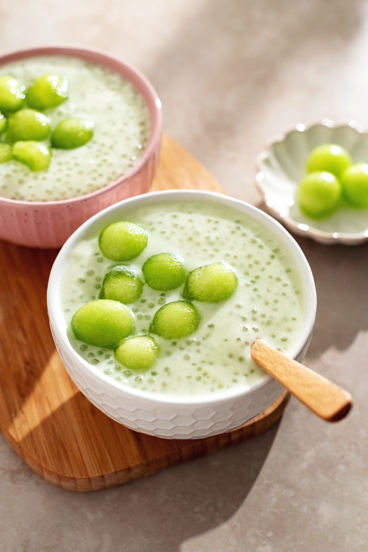 two bowls filled with green peas on top of a wooden tray next to another bowl