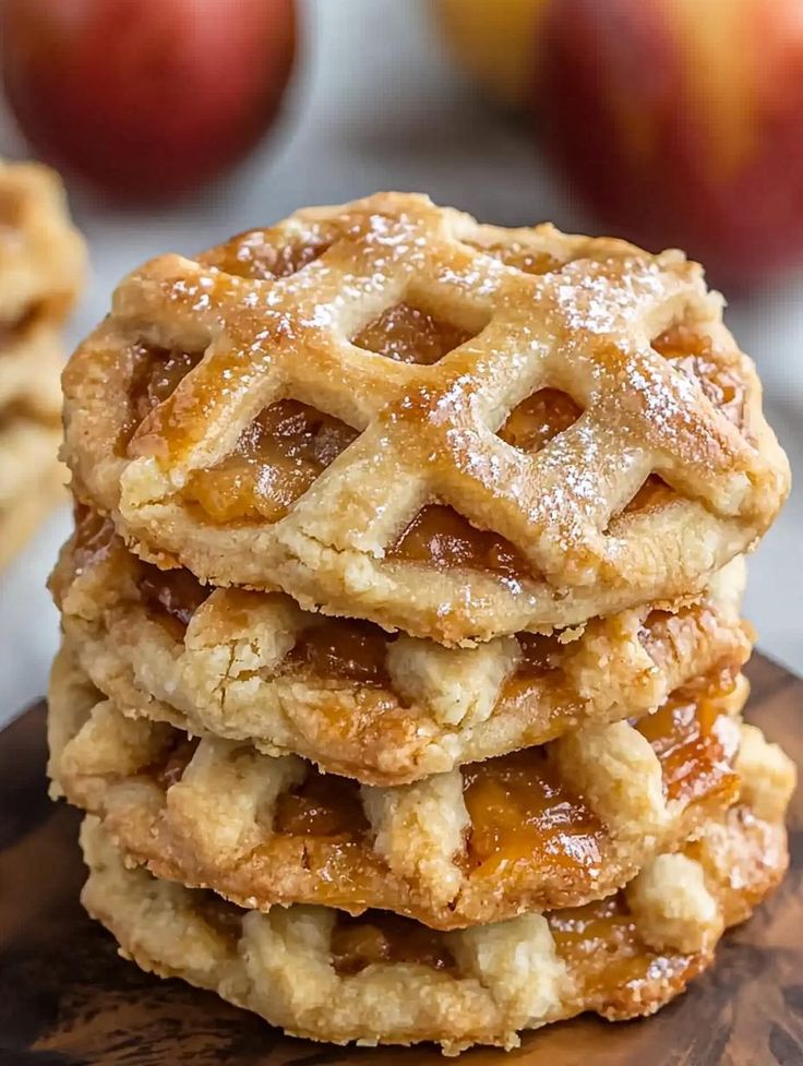 stack of apple pie cookies on top of a wooden cutting board with apples in the background