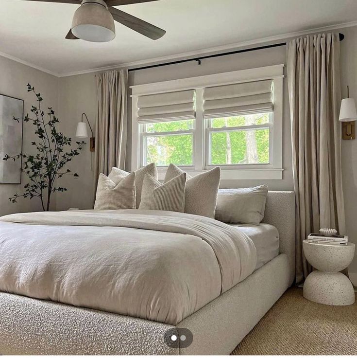 a white bed sitting in a bedroom next to two windows with drapes on them