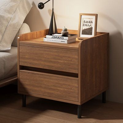 a nightstand with two books on it next to a bed