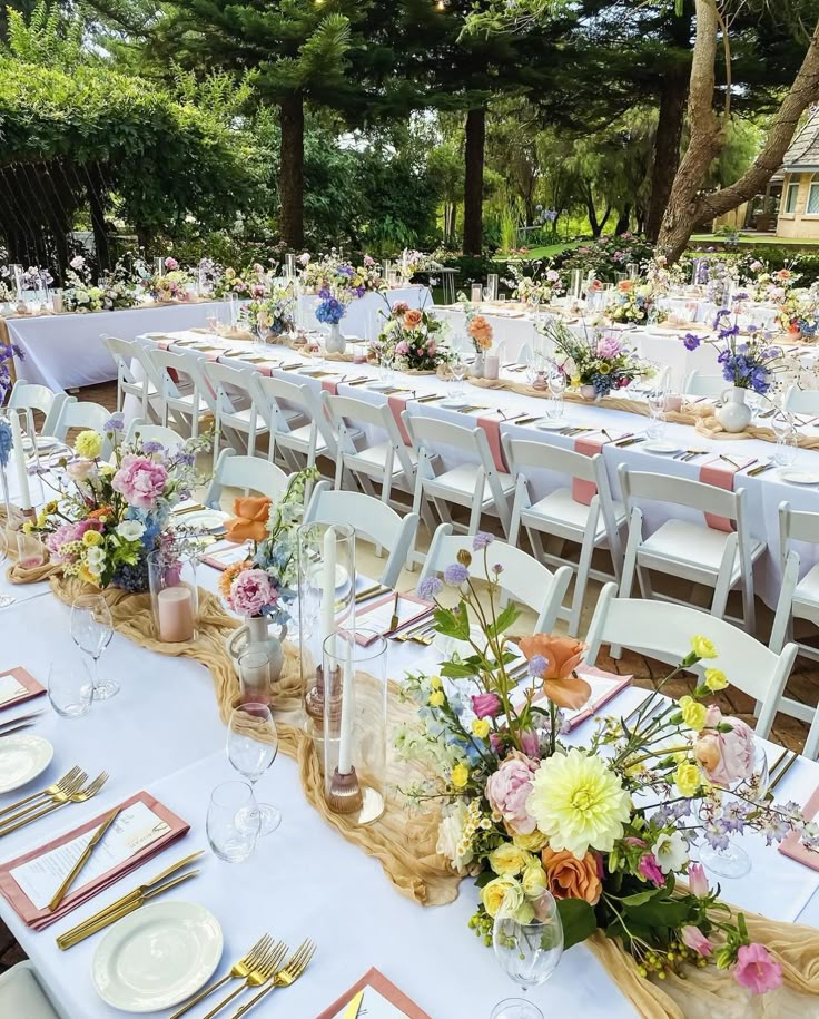 a long table is set up with flowers and place settings for an outdoor wedding reception