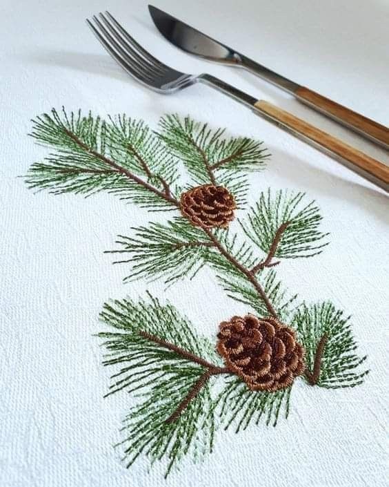 pine cones and needles are embroidered onto napkins with silverware on the table next to them