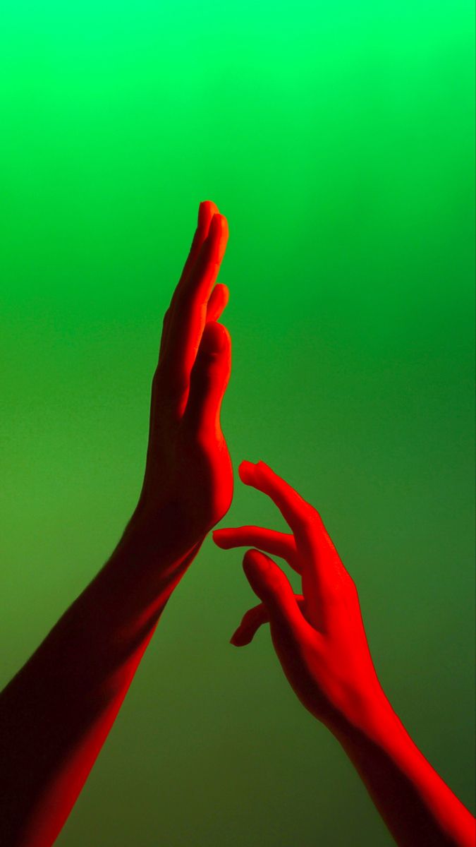 two hands reaching up to each other in the air against a green and red background