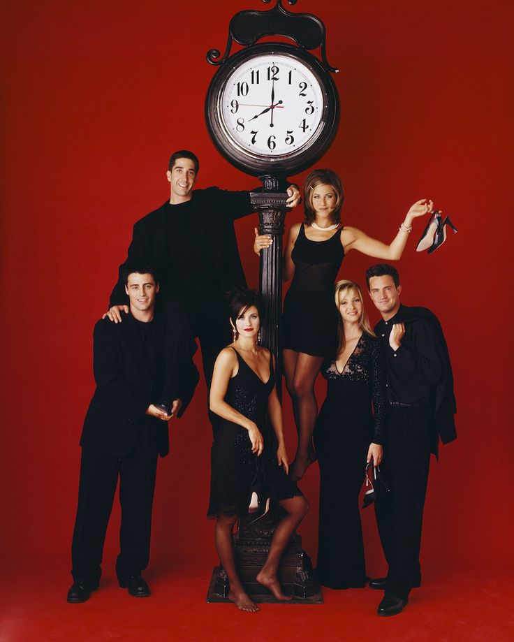 a group of people standing next to a clock on top of a red wall in front of a red background