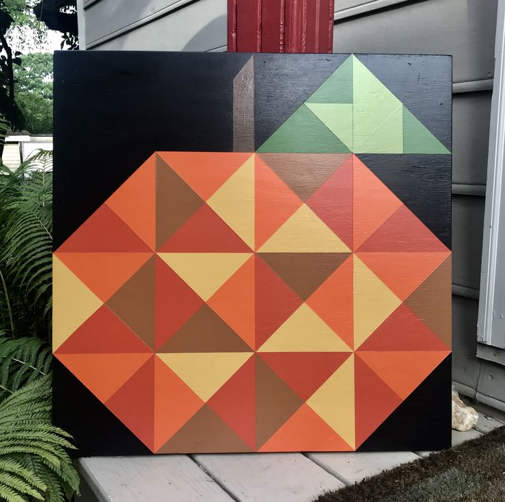 an orange and green abstract painting on a wooden block in front of a gray house