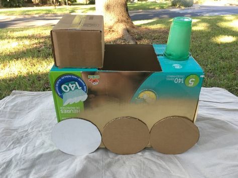 an open cardboard train box sitting on top of a white cloth covered ground next to a tree