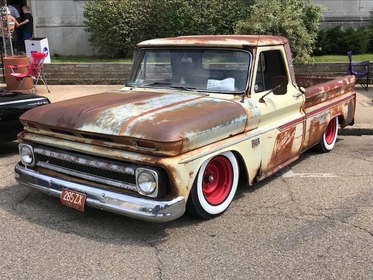 an old rusted truck parked in a parking lot next to other cars and people