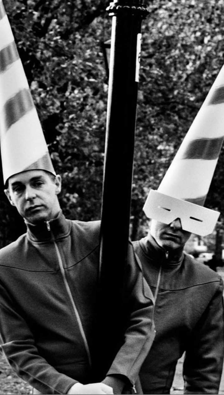 black and white photograph of two men wearing paper hats on their heads, one holding a pole