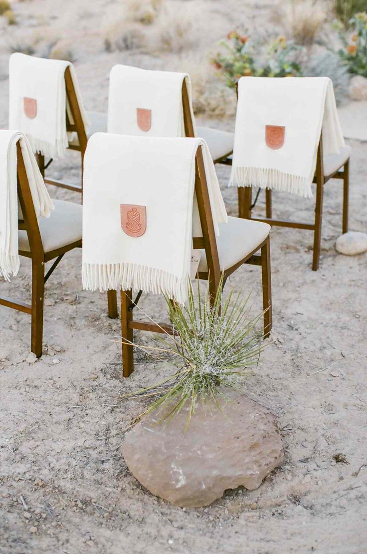 four chairs with blankets on them sitting in the sand next to a rock and plant