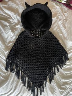 a crocheted black ponchle is laying on a white sheet and has a hood over it