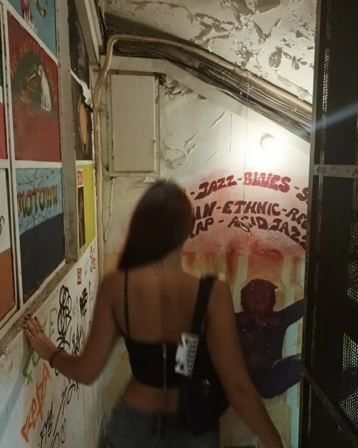 a woman standing in front of a wall covered with posters and writing on the walls