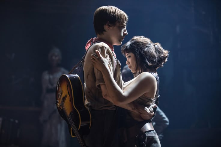 a man holding a woman in his arms while standing next to him with a guitar