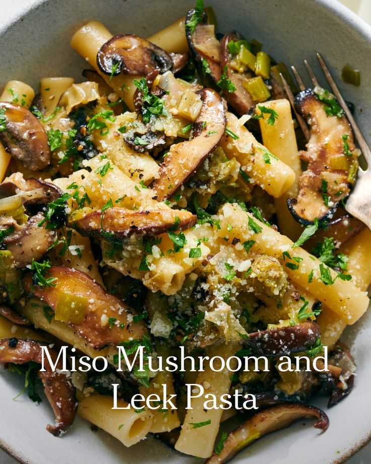 a white bowl filled with pasta covered in mushrooms and parsley next to a fork