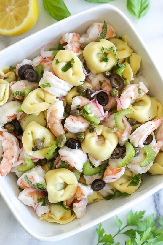 a white bowl filled with pasta salad next to lemon wedges and cilantro