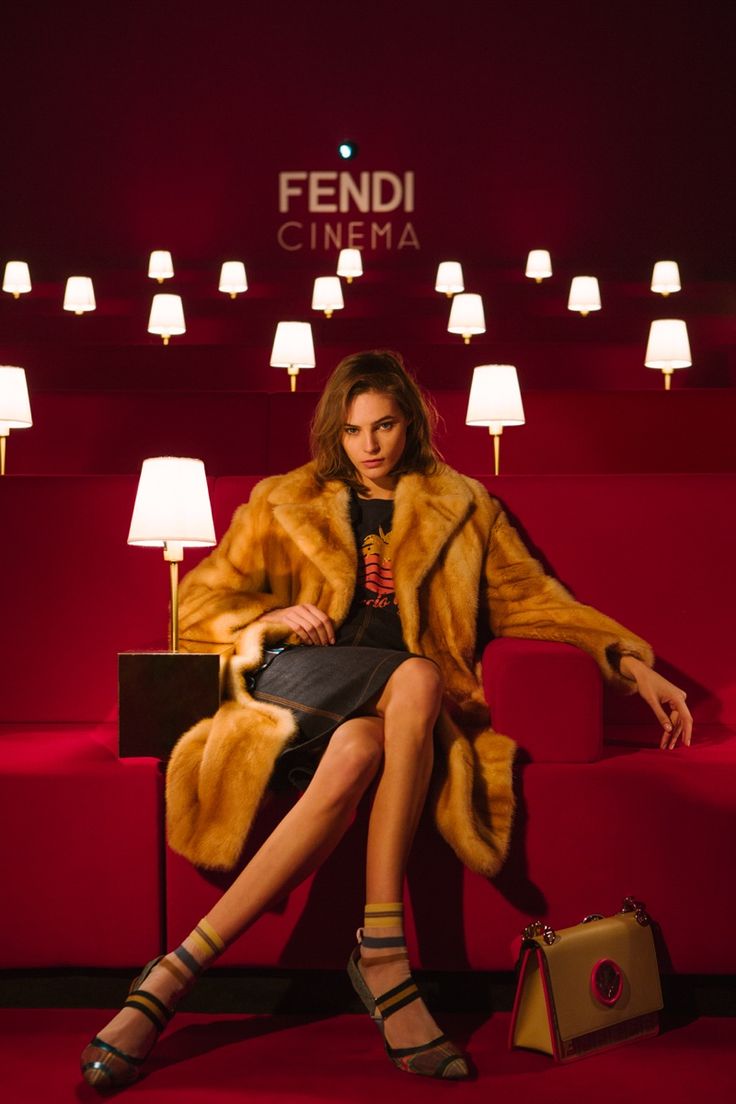 a woman in a fur coat sitting on a red couch next to two lamps and a purse