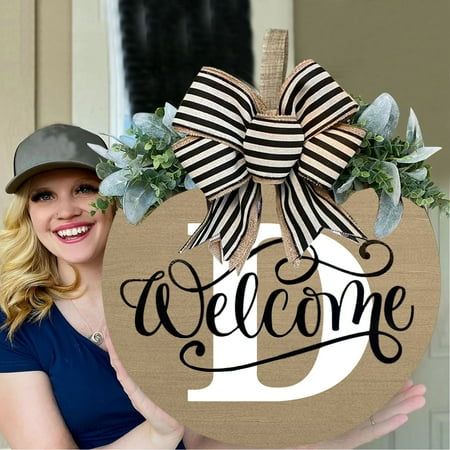 a woman holding up a welcome sign with a bow on it's front door