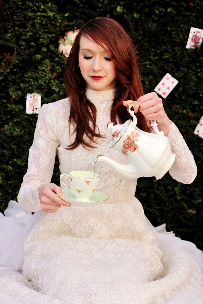 a woman in a white dress is holding a teapot and playing cards with her hands