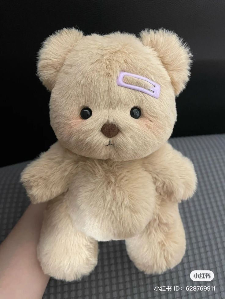 a teddy bear with a pink ribbon on it's head sitting in someones lap