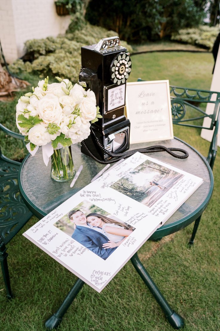 a table with flowers and an old fashioned camera on it, sitting in the grass