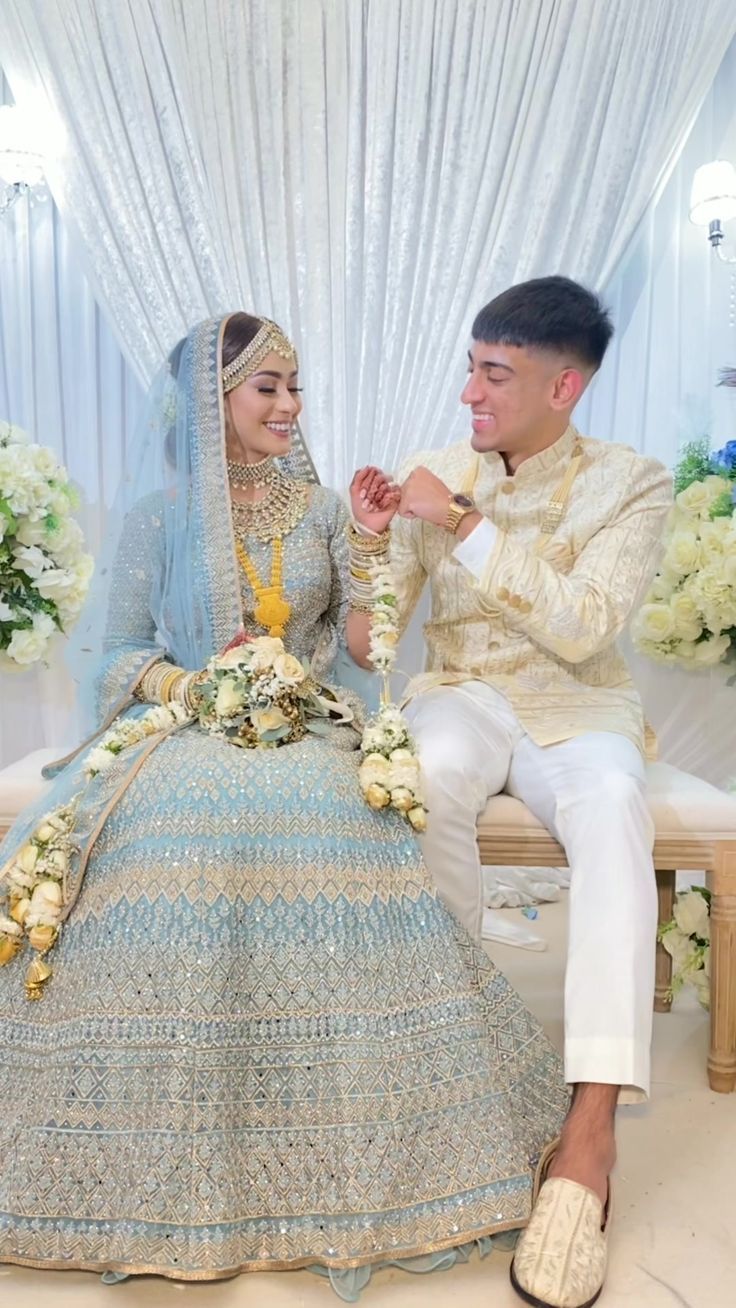 a bride and groom sitting on a bench in front of white floral arrangements at their wedding