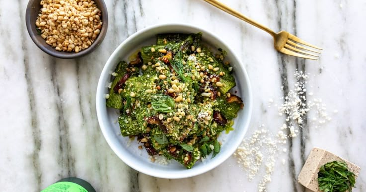 a white bowl filled with food next to a green sprout and two gold spoons