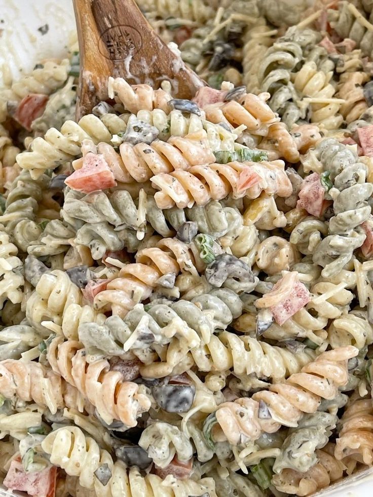 a pasta salad in a white bowl with a wooden spoon