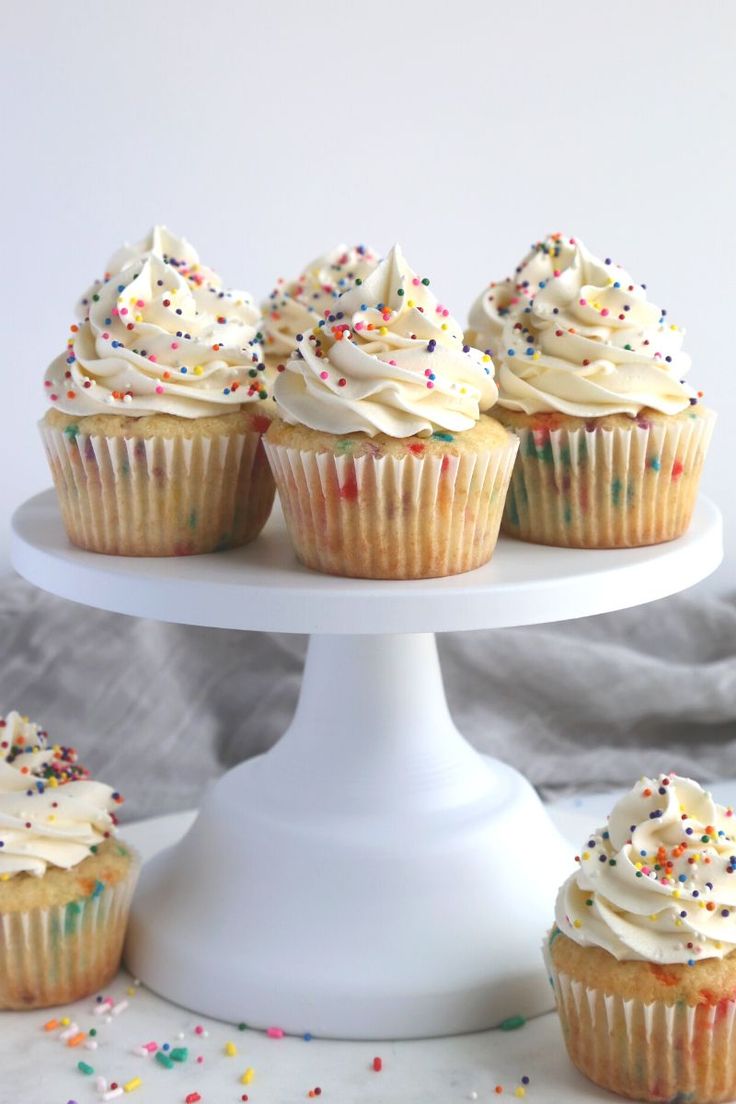 cupcakes with white frosting and sprinkles on a cake stand