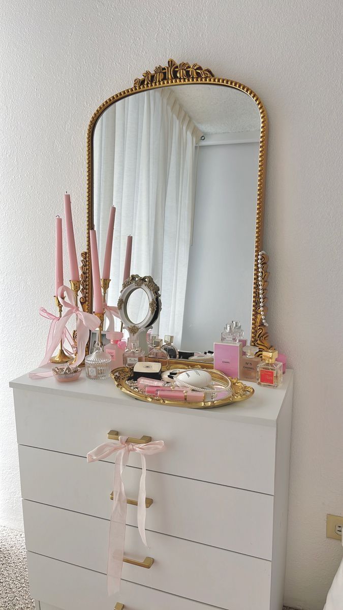 a white dresser topped with a mirror and lots of pink items on top of it