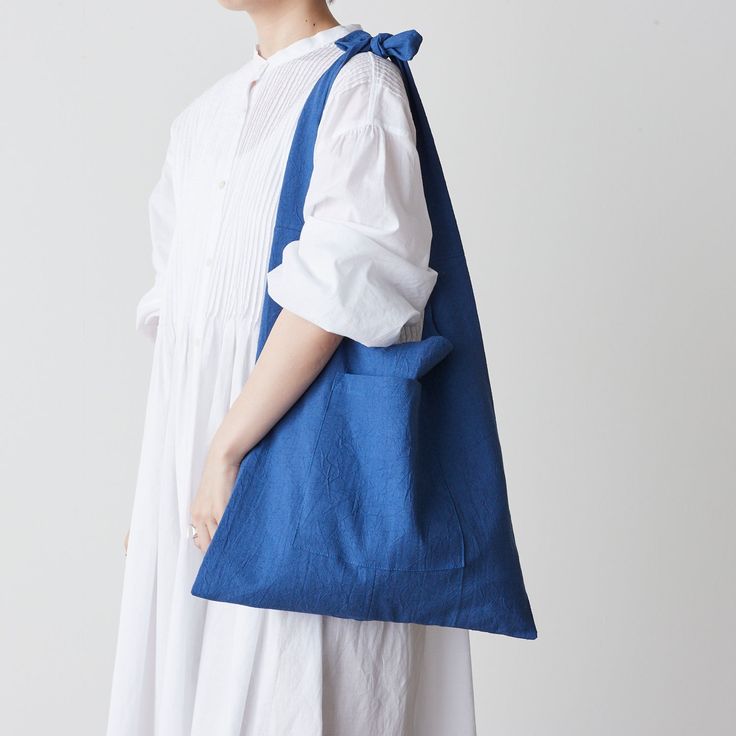 a woman in white dress carrying a blue tote bag with an attached shoulder strap