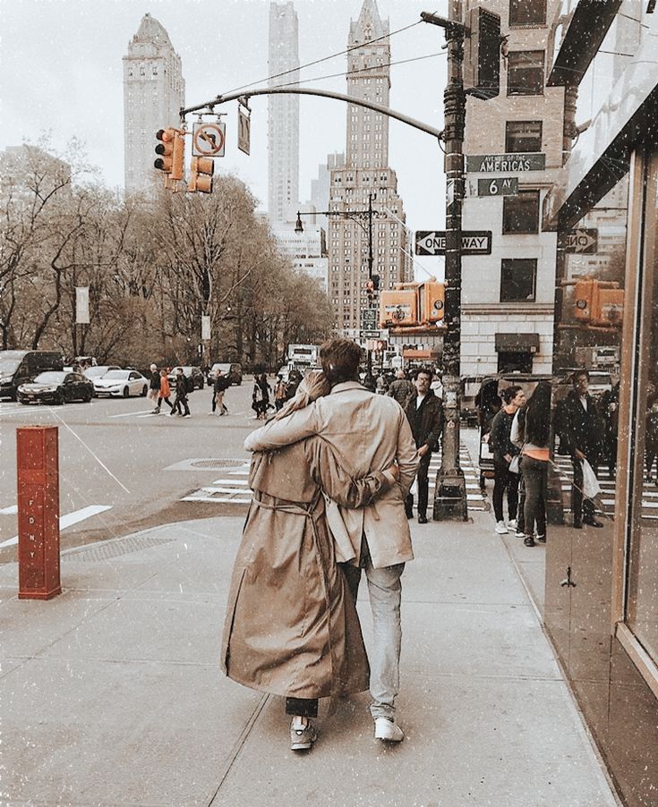 a man and woman walking down the sidewalk in front of a traffic light on a rainy day